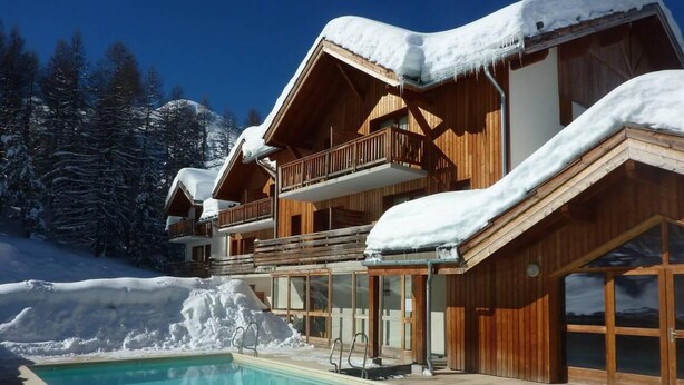 Un chalet en bois doté d’une piscine, entouré d’arbres couverts de neige et surplombant un ciel dégagé.
