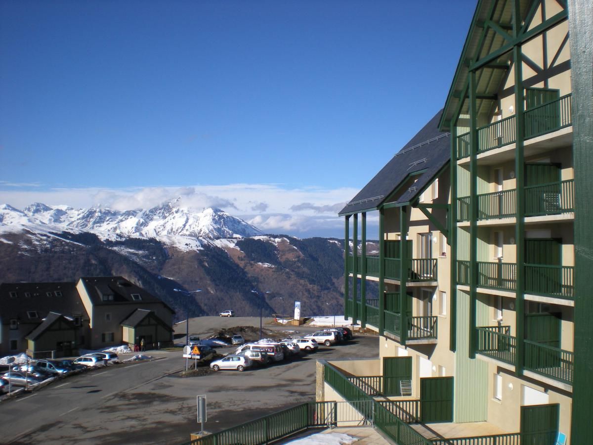 Un hotel con vista a la montaña, estacionamiento y fachada de edificio verde.