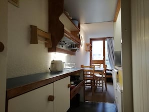A compact kitchen with a toaster, a sink, and a dining area with chairs and a table.