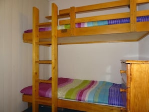 A bunk bed with a ladder, a wooden dresser, and a striped blanket.