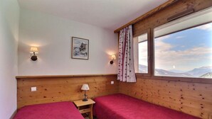 A room with two beds, a small table, wall-mounted lamps, a framed picture, and a window with a view. - 10m from ski slopes, 5th floor, balcony, 33m², Méribel-Mottaret (Méribel - Les Allues)