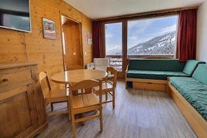 A wooden interior with a round table, chairs, a sofa, and a view of a snowy landscape through large windows.