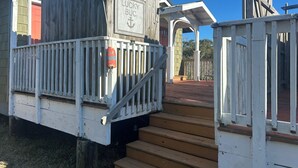 A wooden deck with a staircase leading to a covered area. - The Lucky Buc-Pet friendly cottage perfect for a couple or small family. (Ocracoke)