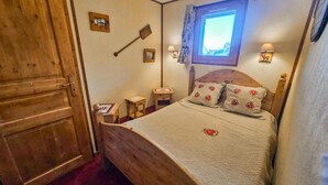 A cozy bedroom with a wooden bed, a window with a view, a wooden door, and a small bedside table with a lamp. - 10m from ski slopes, Ground floor, view mountain, balcony, tv, ski locker, 30m², Les Menuires (Les Menuires)
