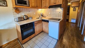 A compact kitchen with wooden cabinets, a microwave, a toaster, a kettle, a dishwasher, and a small refrigerator. - 10m from ski slopes, Ground floor, view mountain, balcony, tv, ski locker, 30m², Les Menuires (Les Menuires)