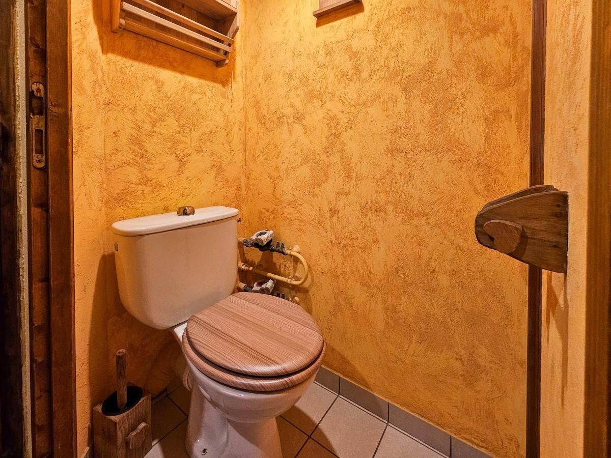 A small bathroom with a toilet, a wooden door, and a tiled floor.
