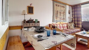 Un salon chaleureux avec une table à manger dressée pour deux personnes, un canapé et une fenêtre donnant sur la campagne.
