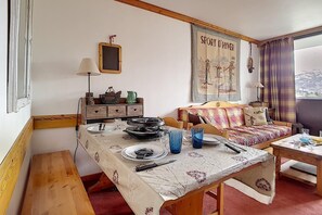 A cozy living room with a dining table set for two, a sofa, and a window with a view of the countryside. - 50m from resort center, 8th floor, balcony, tv, ski locker, 36m², Les Menuires (Les Menuires)