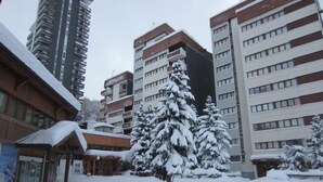 Un paysage urbain enneigé, avec des immeubles à plusieurs étages, un abribus et des arbres couverts de neige.