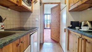 Une cuisine avec des meubles en bois, un plan de travail et une vue sur l’extérieur grâce à une porte ouverte.