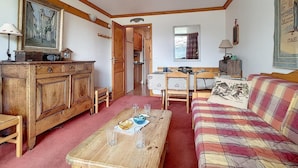 Un salon chaleureux avec un meuble en bois, un canapé à carreaux, une table à manger avec des verres et un tableau accroché au mur.