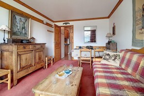 A cozy living room with a wooden cabinet, a plaid sofa, a dining table with glasses, and a painting on the wall. - 50m from resort center, 8th floor, balcony, tv, ski locker, 36m², Les Menuires (Les Menuires)