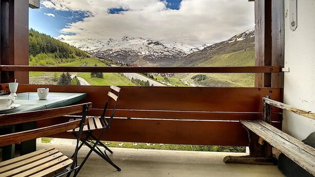 Un balcon avec un banc et une table en bois, donnant sur un paysage montagneux sous un ciel dégagé.