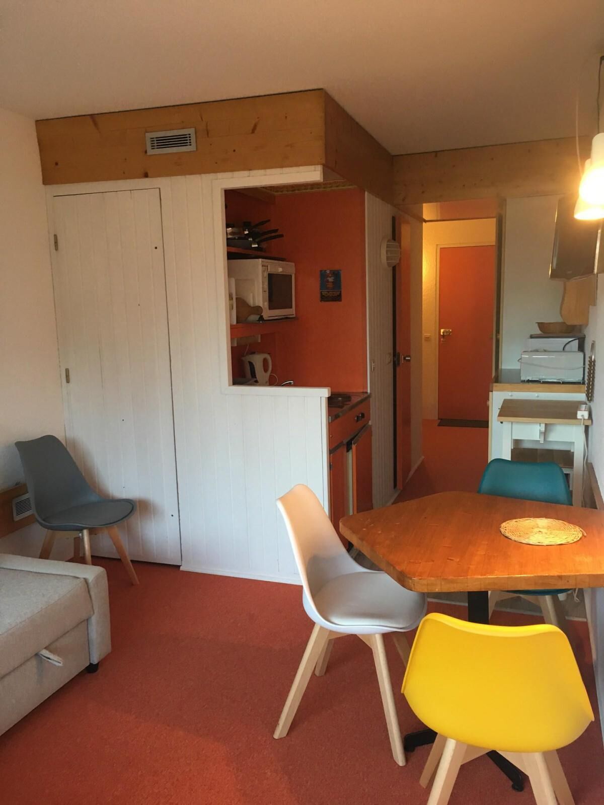 A compact living space with a dining area featuring a wooden table and four chairs, a kitchenette with a microwave, and a small seating area with a sofa and two chairs.