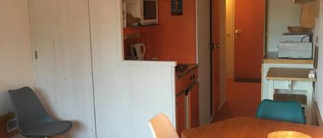 A compact living space with a dining area featuring a wooden table and four chairs, a kitchenette with a microwave, and a small seating area with a sofa and two chairs.