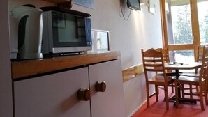 Una kitchenette con microondas, tostadora y hervidor sobre una encimera de madera. Hay una mesa de comedor con sillas y una ventana con vistas a árboles.
