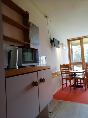 Pieni keittiönurkkaus, jossa on mikroaaltouuni, leivänpaahdin ja vedenkeitin, ja kaikki sijoitettu puiseen työtasoon. Nurkkauksessa on ruokapöytä tuoleineen ja ikkuna, josta avautuu näkymä puita kohti.