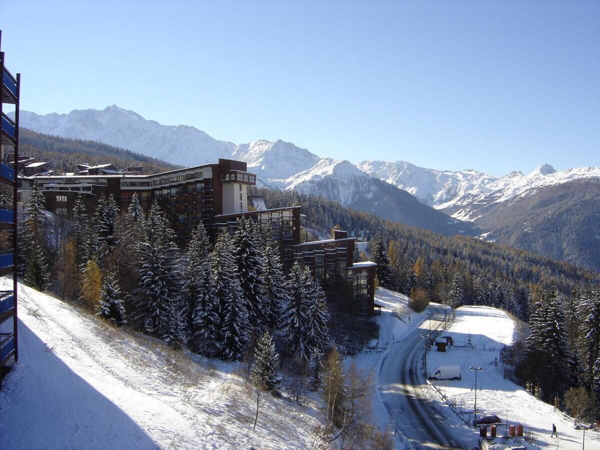 A snow-covered mountain resort with a ski slope, buildings, and a clear view of the mountains.