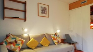 Una sala de estar con un sofá, dos cojines amarillos, una silla y un cuadro en la pared.