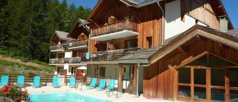 A wooden chalet with a swimming pool, multiple balconies, and outdoor seating.