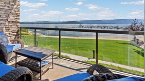 A balcony with wicker furniture, a stone wall, and a view of a marina and mountains. - Master Suite w/Lake Views - Seasons at Sandpoint (Sandpoint)