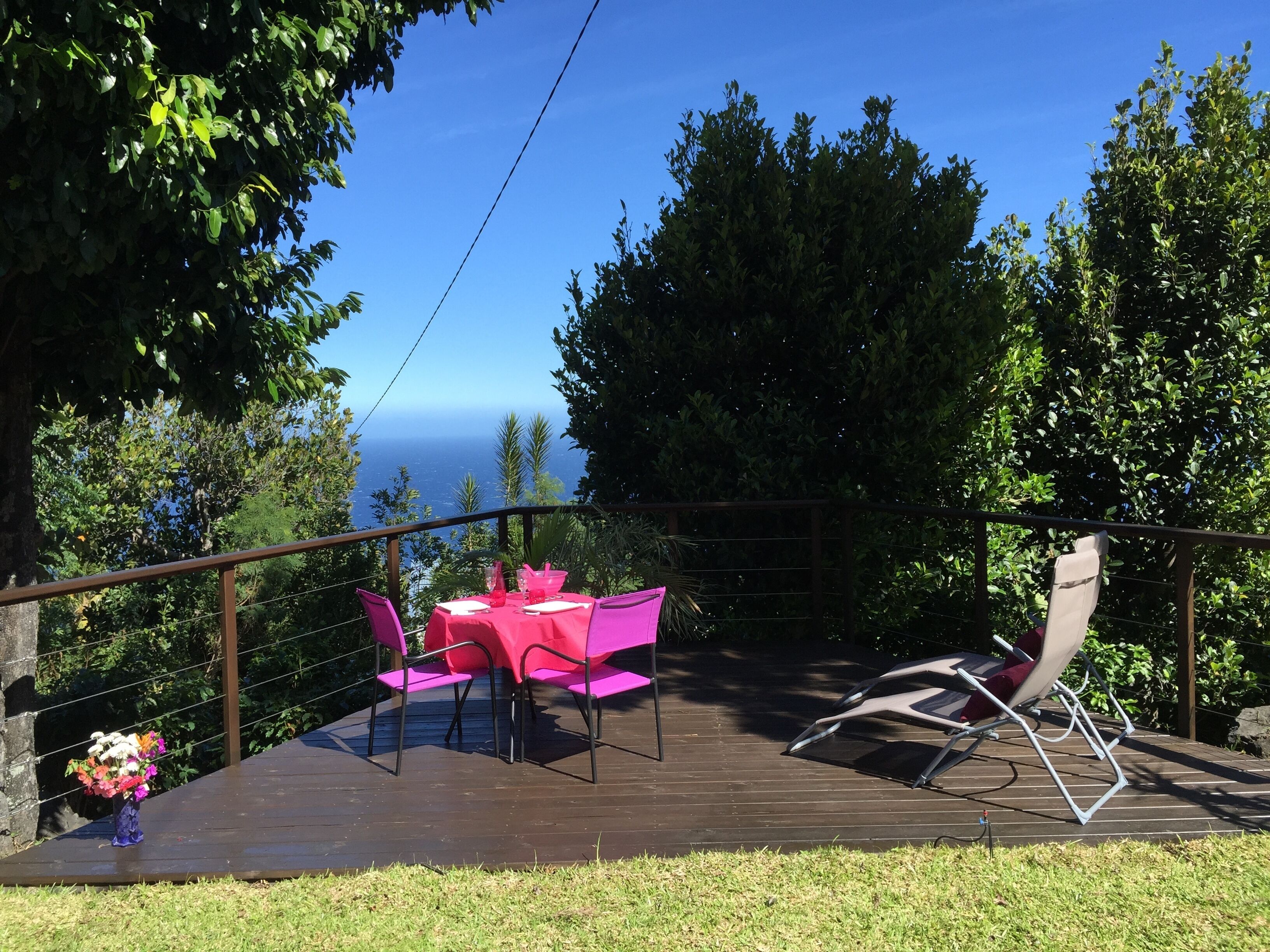 A wooden deck with a table and chairs, overlooking a scenic view of the ocean.