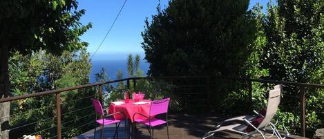 A wooden deck with a table and chairs, overlooking a scenic view of the ocean.