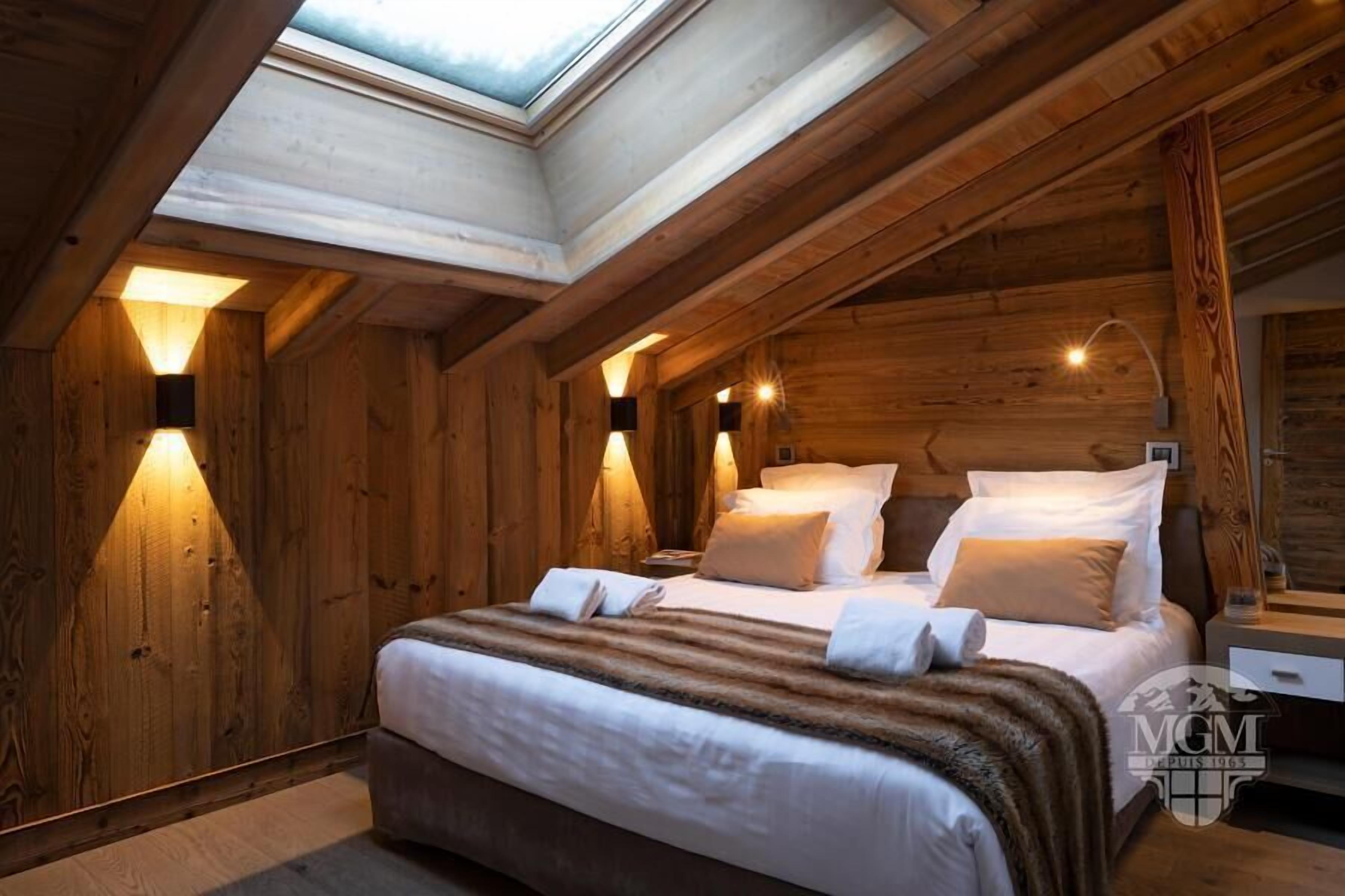 A cozy wooden room with a bed, two bedside tables, and a skylight above.