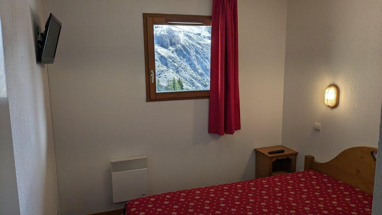 A bedroom with a bed, a window with a view of mountains, a wall-mounted heater, a bedside table with a remote control, and a wall-mounted light fixture.