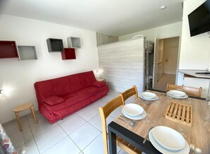 Ein Essbereich mit einem Holztisch, gedeckt für vier Personen, einer roten Couch und einem kleinen Hocker.