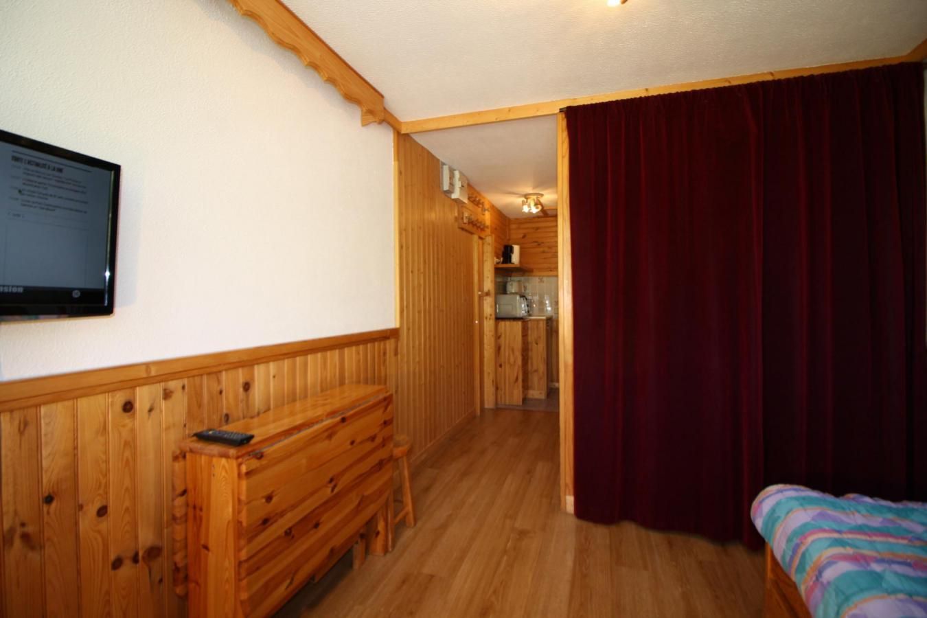 A wooden-paneled room with a bed, a desk, and a television on the wall.