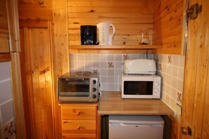 A compact kitchen with wooden cabinets, a toaster, a microwave, and a small refrigerator.