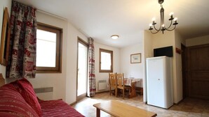 A compact living space with a sofa, a dining table with chairs, a refrigerator, and a chandelier.