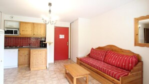 A compact living space with a kitchenette, a red door, a wooden sofa, a wooden table, and a mirror on the wall.