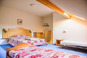 Une chambre avec deux lits, une tête de lit en bois, une petite commode en bois, une chaise et une table de chevet.