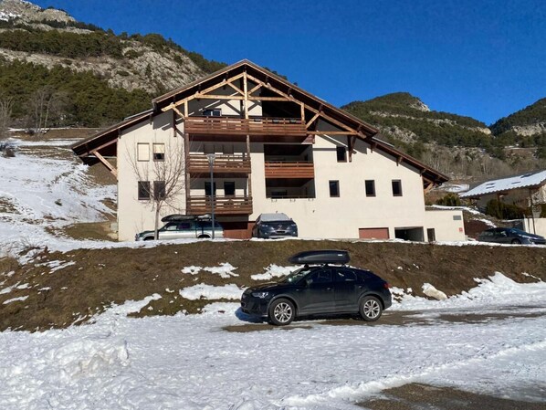 A two-story chalet with a wooden facade, a balcony, and a car parked in front.