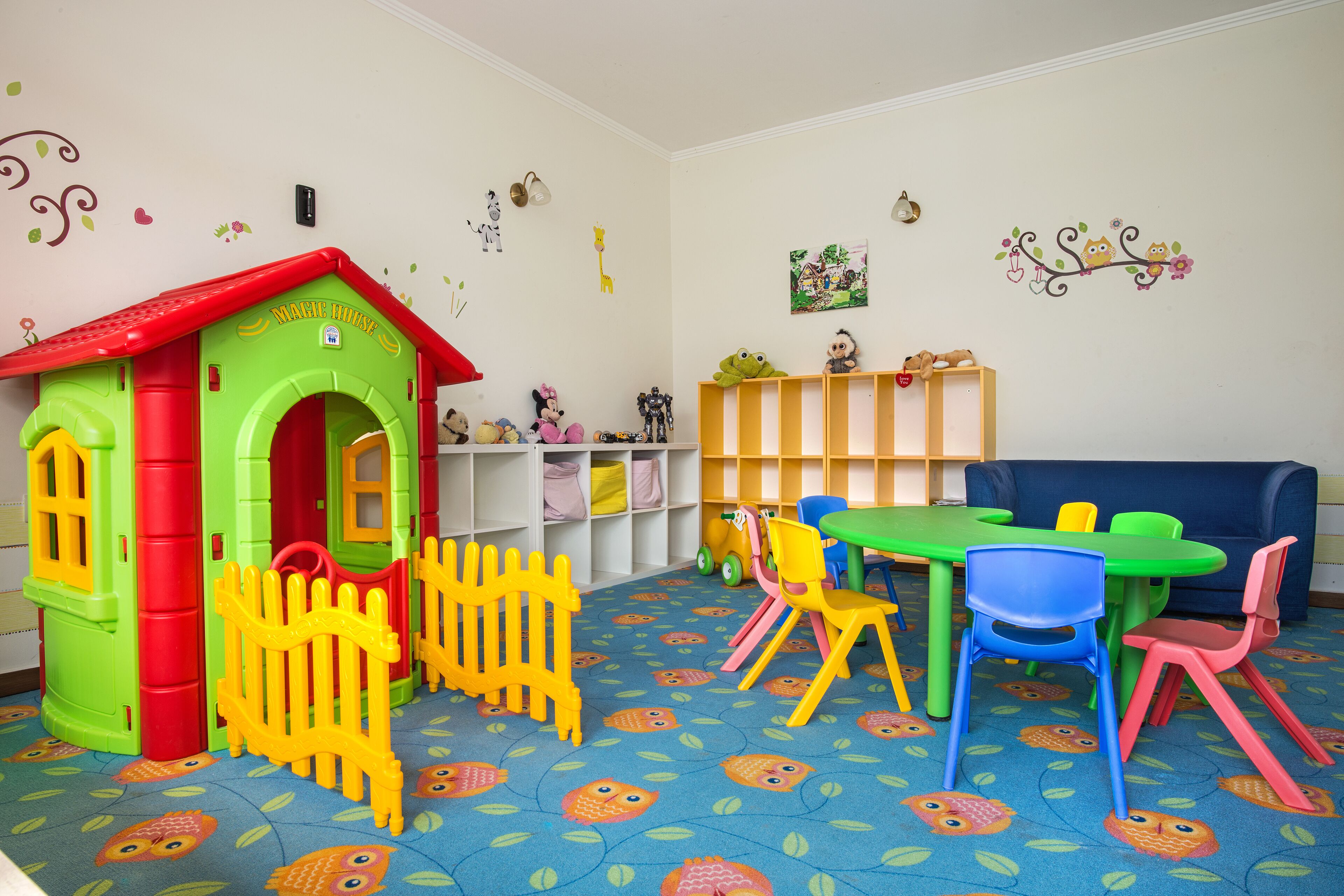 A children's playroom with a playhouse, colorful chairs, a table, and a bookshelf.