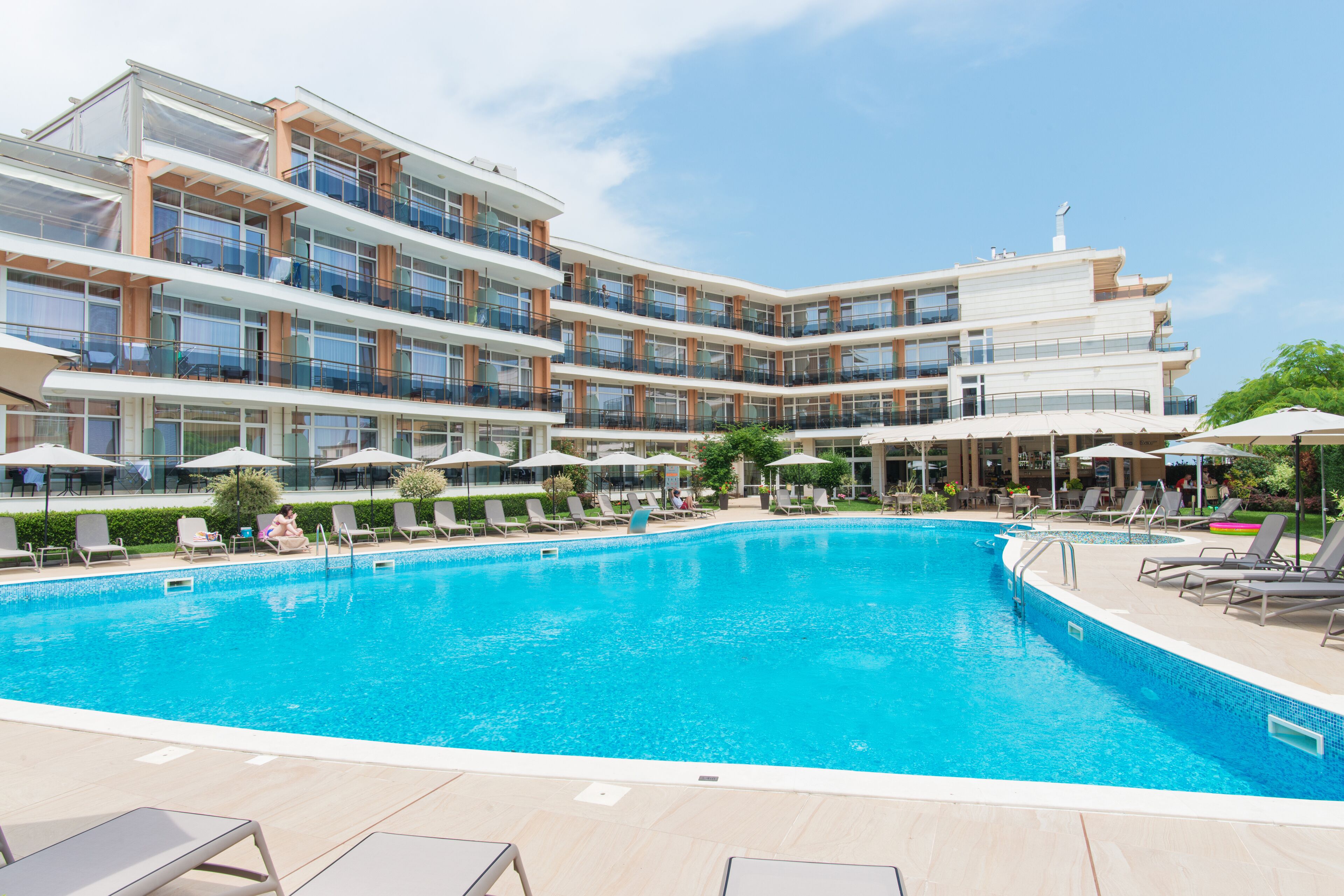 Un hotel moderno con una amplia piscina, varios balcones y zonas de estar al aire libre.