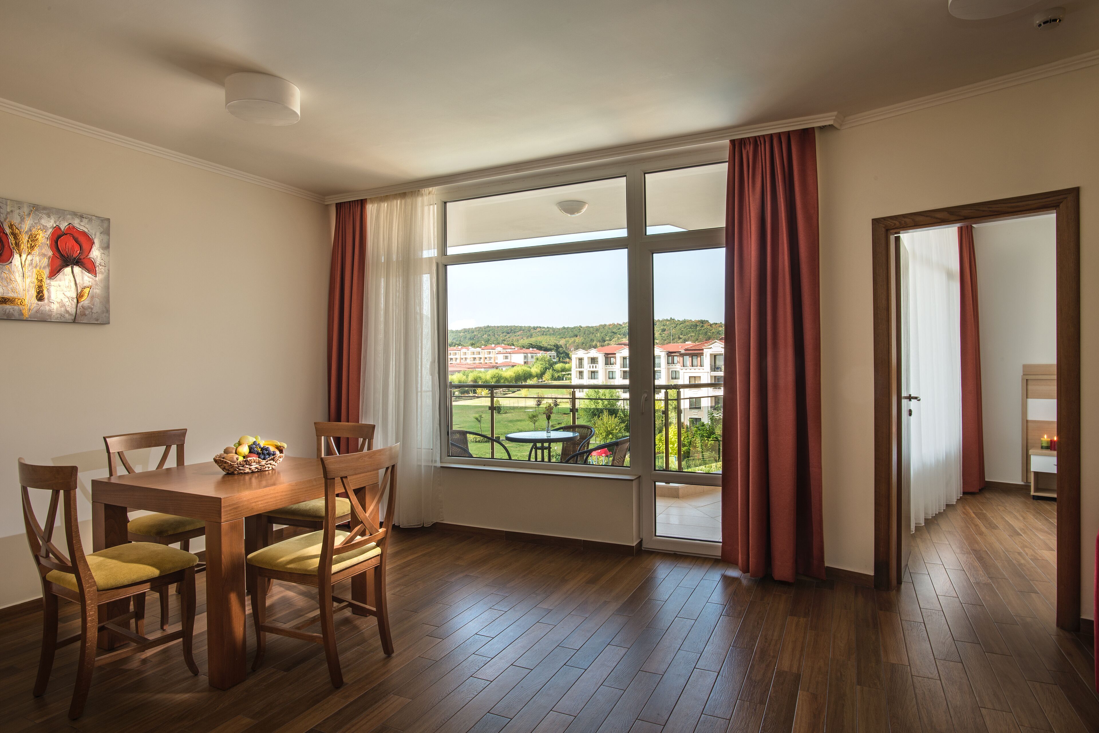 Un comedor con una mesa y sillas de madera, una ventana con cortinas, y vistas a edificios distantes.