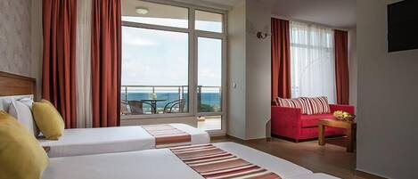 Habitación de hotel con dos camas, un sofá rojo, una mesita y un balcón con vistas.