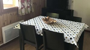 Een eethoek met een tafel bedekt met een tafelkleed met stippen, omringd door vier donkere stoelen. Een flatscreen televisie hangt aan de muur boven de tafel.