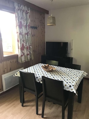 A dining area with a table covered in a polka dot tablecloth, surrounded by four dark chairs. A flat-screen TV is mounted on the wall above the table. - 200m from shops, 1st floor, view valley, swimming pool, sauna, hammam, balcony, ski locker, 33m² (Les Orres)