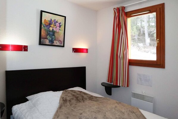 A bedroom with a bed, a painting, a window with curtains, and a wall-mounted shelf.