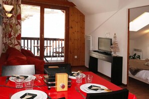 A room with a dining table set for two, a television on a stand, and a bed with a teddy bear. - Ski-in/ski-out & foot of the slopes, 3rd floor, view swimming pool, swimming pool, sauna, hammam (Les Orres)