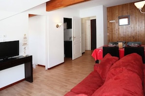 A living room with a red sofa, a TV on a black stand, and a wooden ceiling.