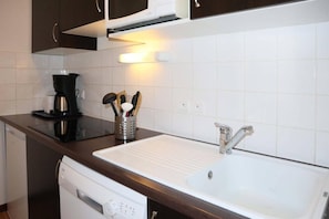 A kitchen with a white sink, dark countertops, and a coffee maker.