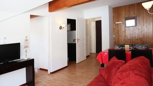 Un salon avec un canapé rouge, un téléviseur posé sur un meuble noir et un coin repas comprenant une table et des chaises rouges.