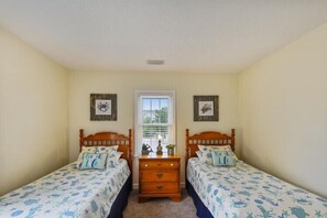 A bedroom with two single beds, a dresser, and a window with blinds.
