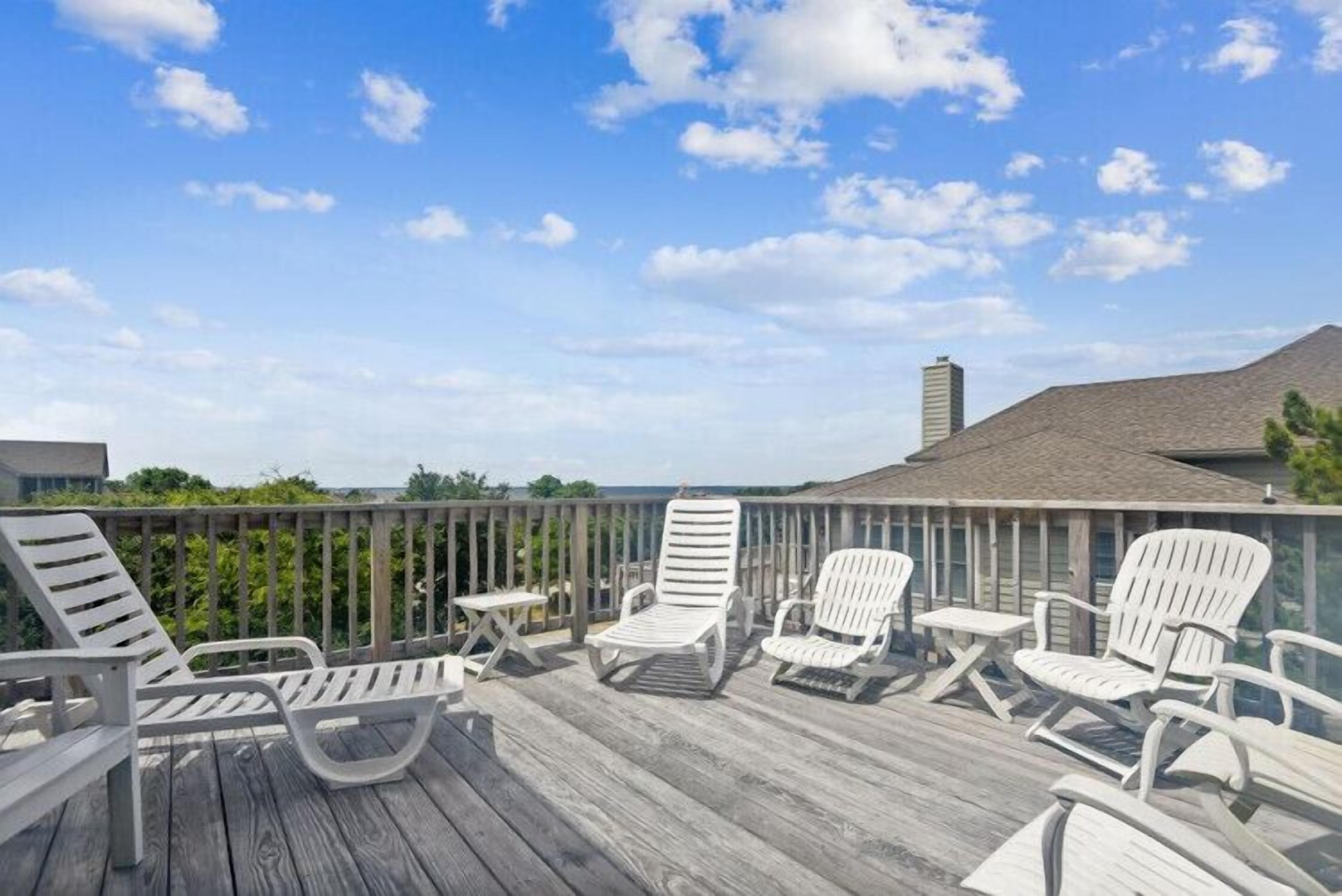A wooden deck with lounge chairs and a table, overlooking a body of water.
