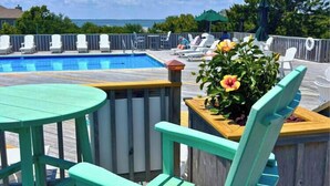 Área de piscina com deck de madeira, uma mesa redonda e cadeiras.